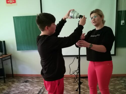 Uczeń ósmej klasy, pod nadzorem pani fotograf, dokręca świetlówkę do statywu