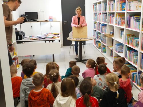 Dzieci słuchają opowiadania bibliotekarki o pracy w bibliotece